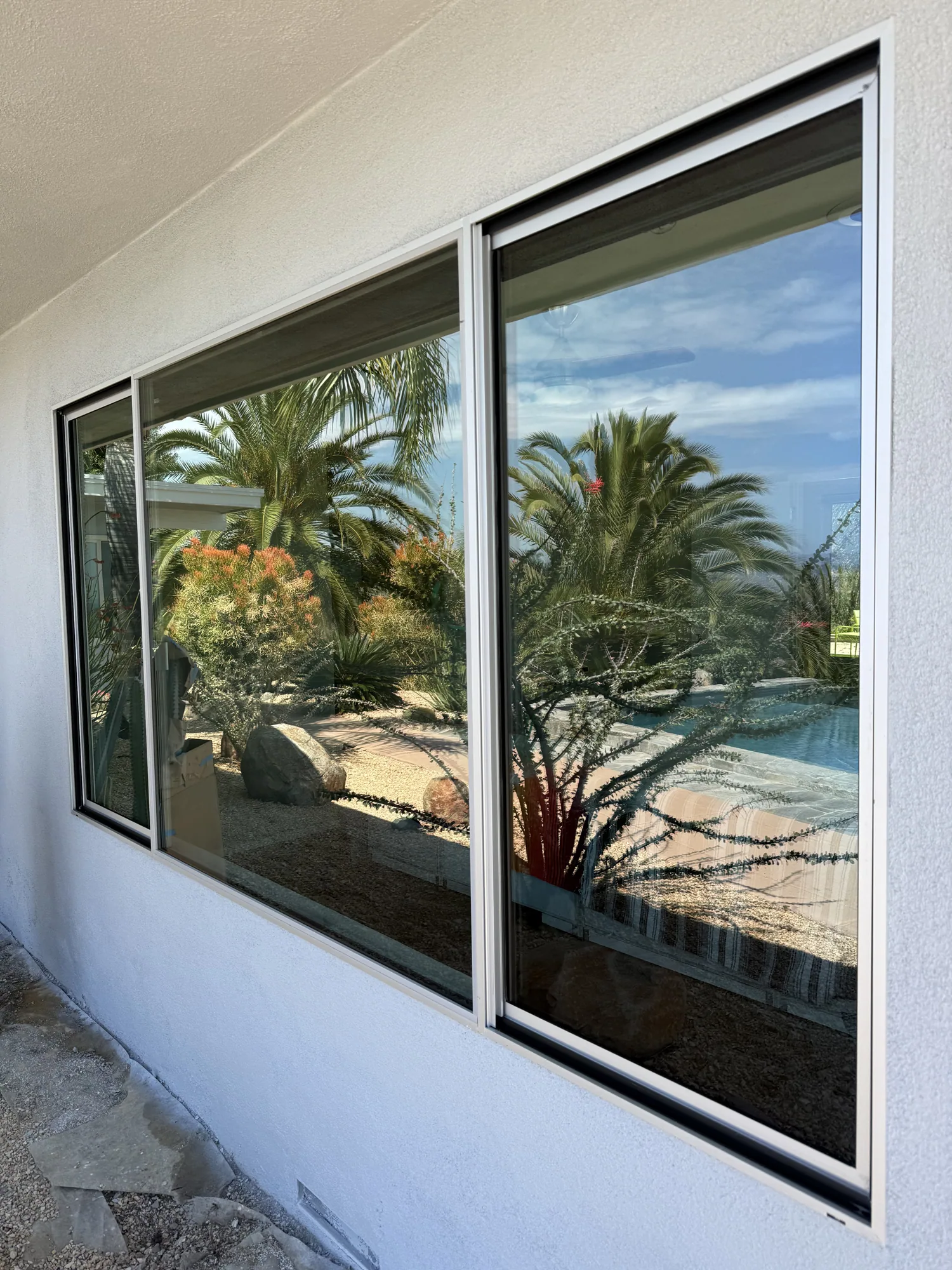 A cleaned sliding glass window on a white stucco wall, reflecting palms and a swimming pool.