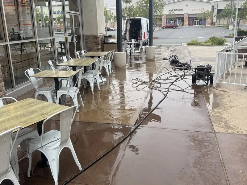 A shopping center walkway mid wash, wet concrete and hoses run out to a pressure washer beside the van.