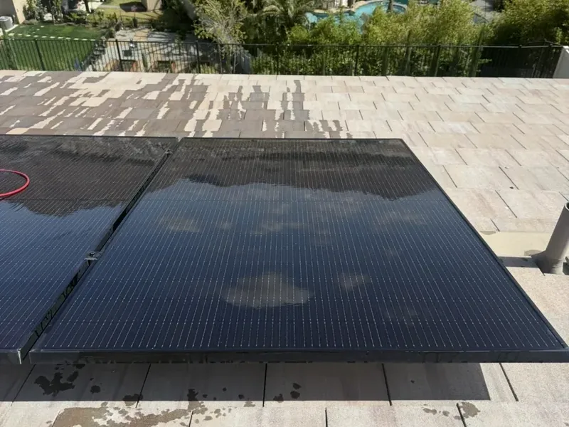 A solar panel on a tile roof, washed clean and still wet, with the neighborhood below.