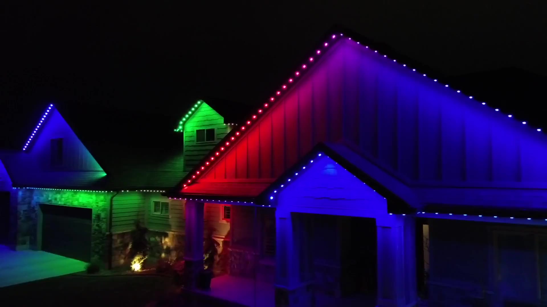 Green-and-stone home at night with the permanent roofline lights set to red, green and blue