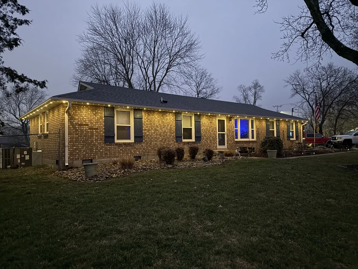 Dusk photo of a single-storey brick ranch with warm permanent lights along the eaves
