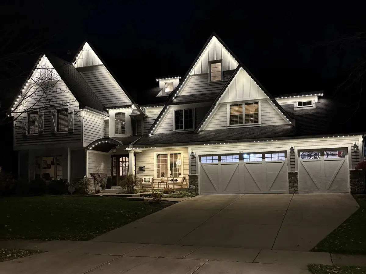 Light-coloured multi-gable home at night with permanent lights along the gables, eaves and garage