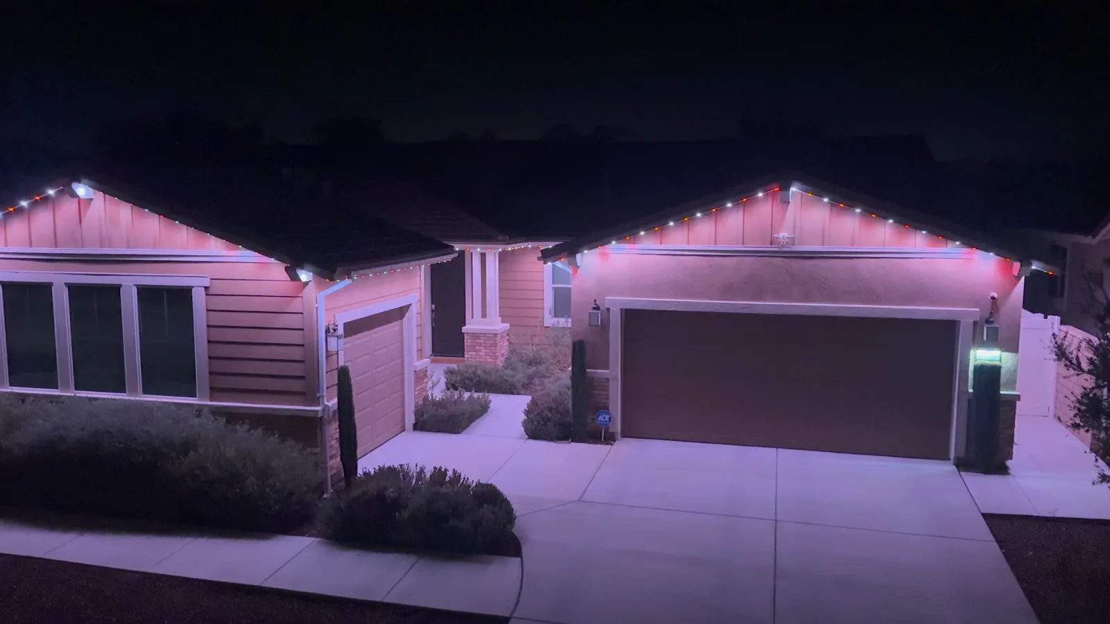Single-storey home at night with the permanent roofline lights on in white and the walls washed pale pink