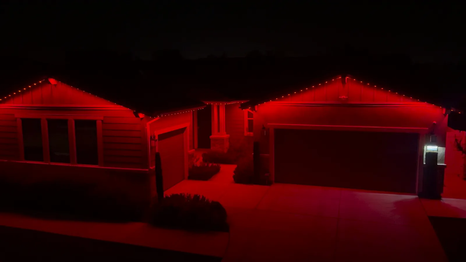 The same home at night with the permanent roofline lights set to red, the walls and driveway lit red