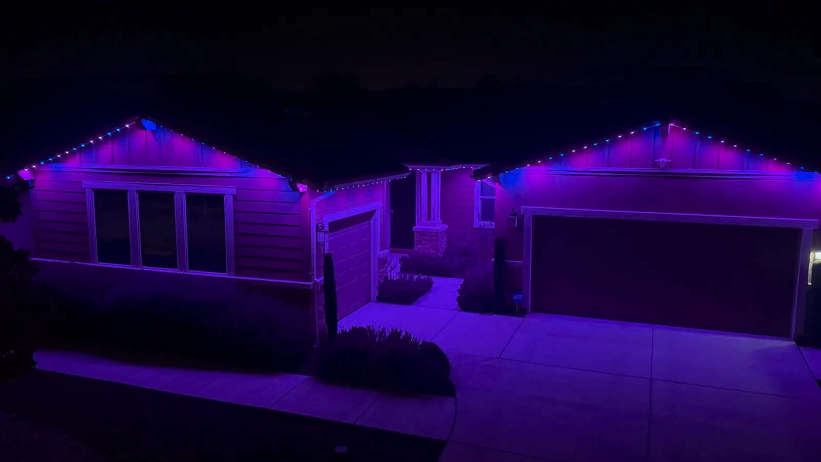 The same home at night with the permanent roofline lights set to blue and purple