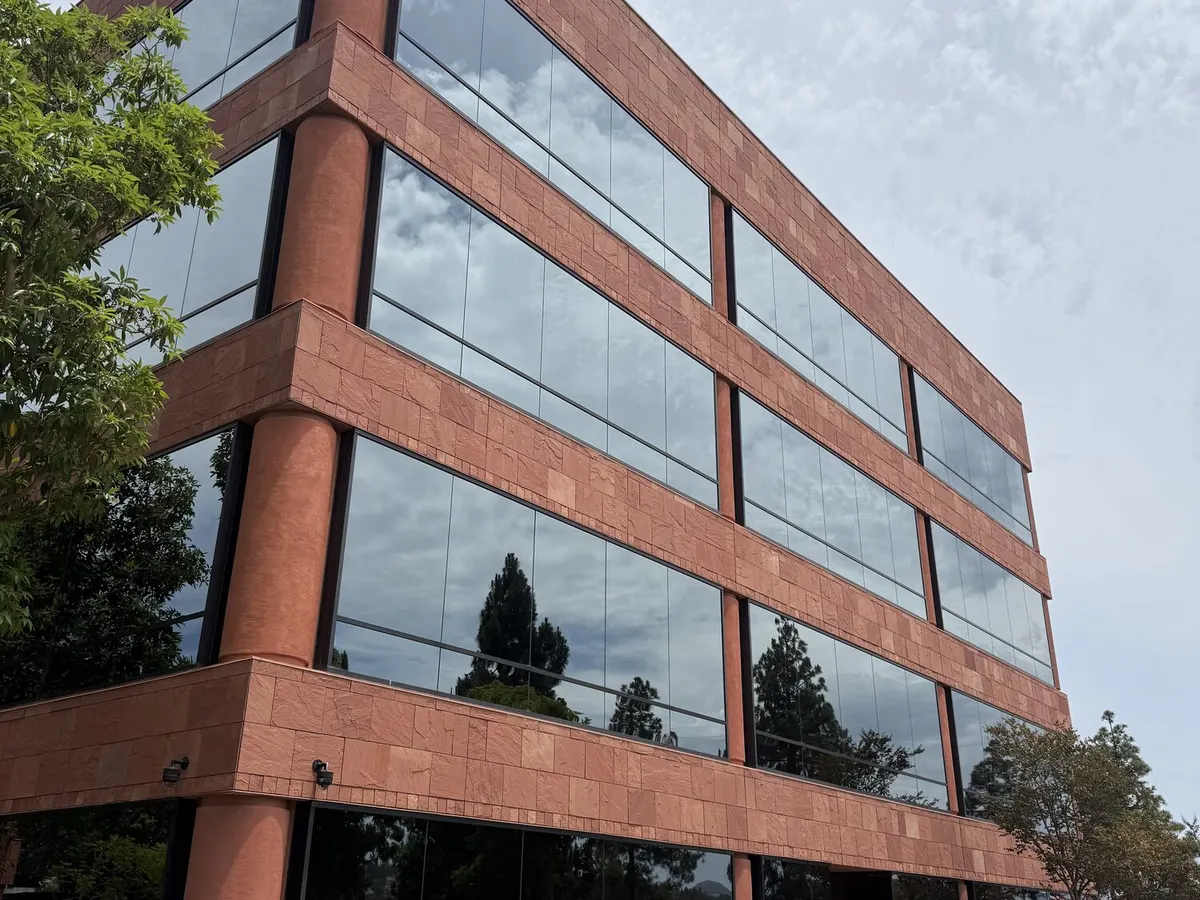 A four story office building in red stone and dark glass, photographed from the parking lot.