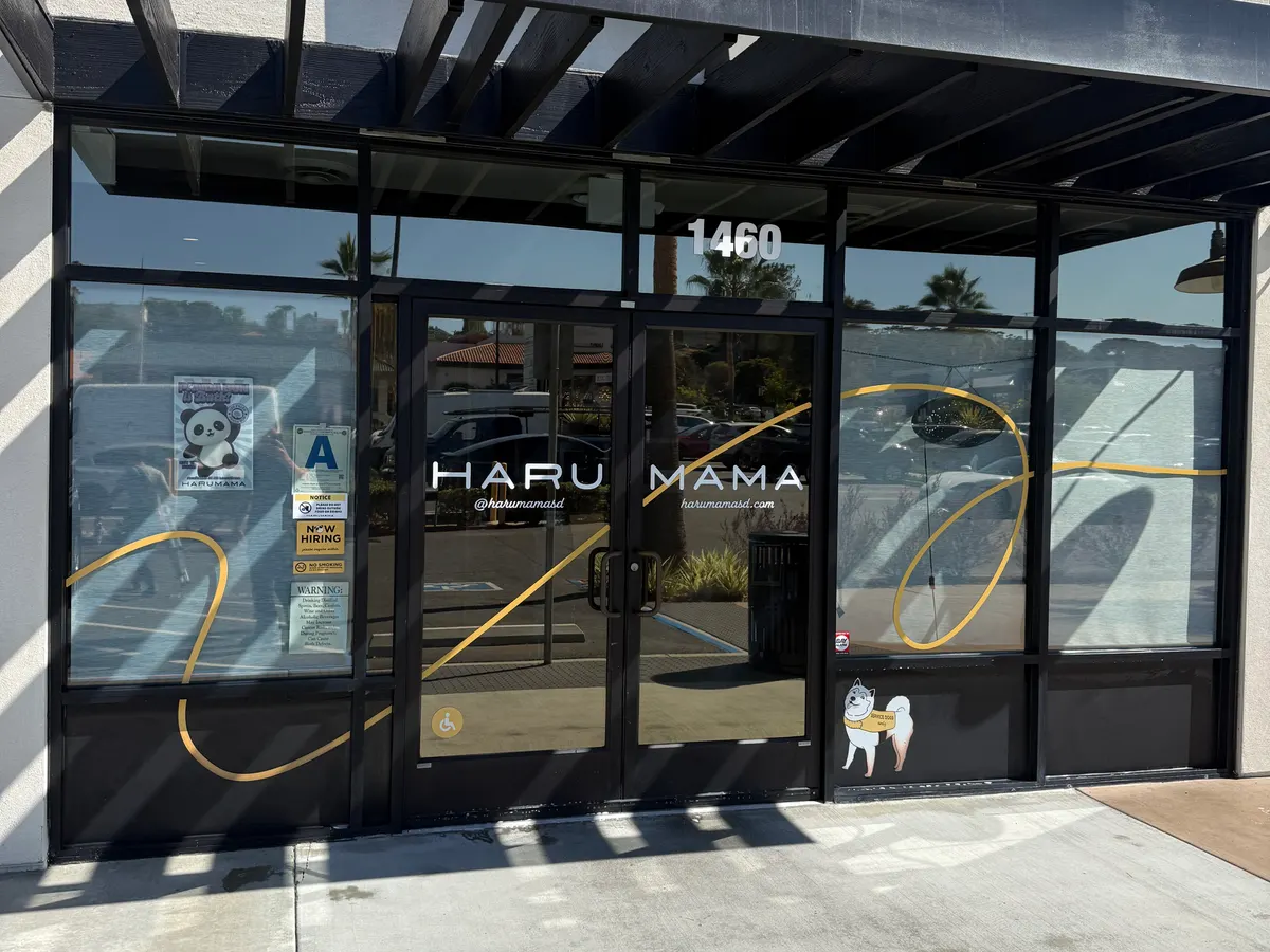 A restaurant storefront with black framed glass doors and a hose run out across the sidewalk.