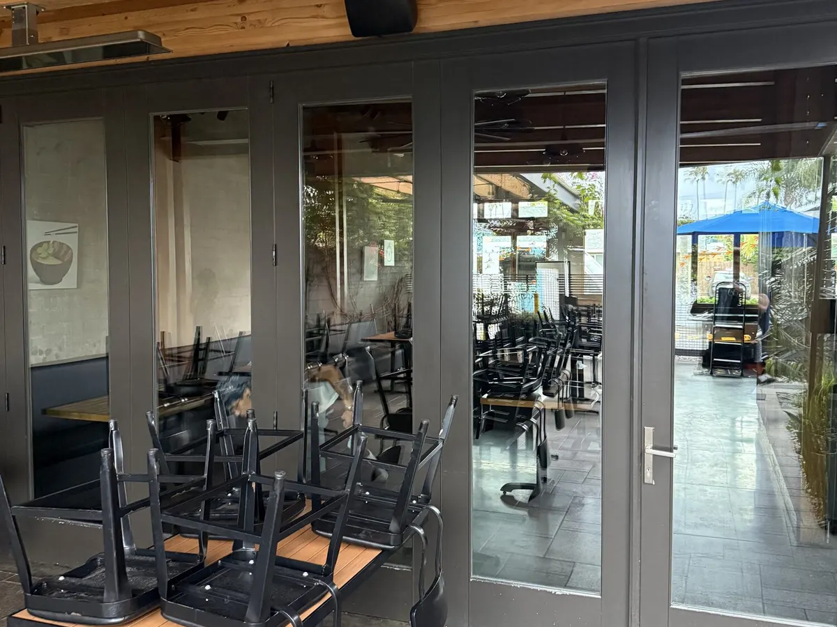 Glass doors under a timber ceiling opening onto a patio, with tables and stacked chairs outside.