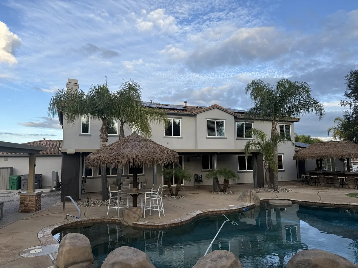 The back of a two story home with palms and a thatched palapa beside a swimming pool.