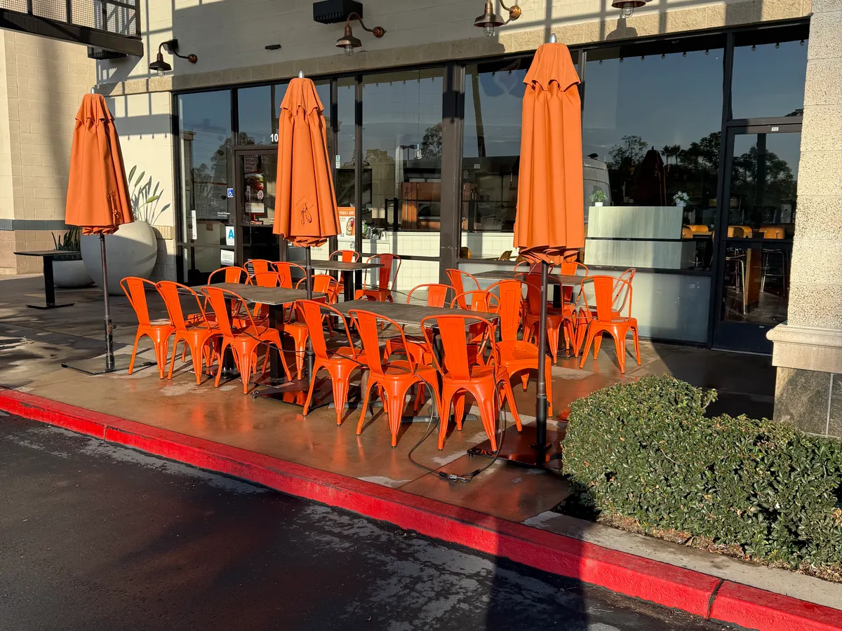 A restaurant patio with orange chairs stacked to one side and the concrete still wet from a pressure wash.