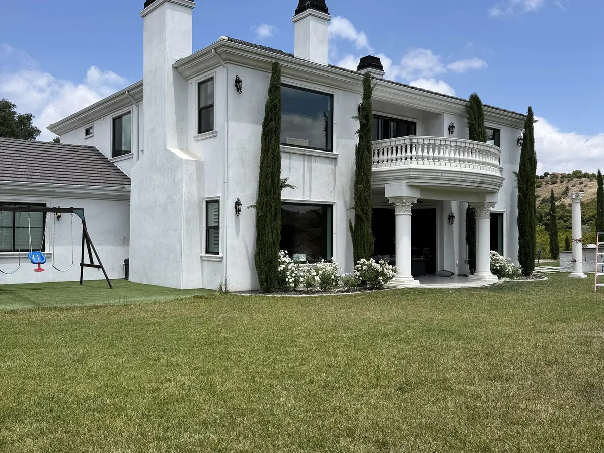 A white two story home with columns and cypress trees, seen across a green lawn.